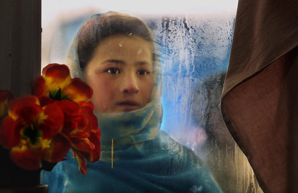 A girl looks through the frosted window of a restaurant, hoping to get leftovers. She begs after school to help out her family. (Kabul, January 13, 2002)