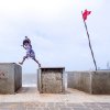 Neenad Arul - A little girl jumps with a steel glass as red flag roars with wind , she stays in the small hut which is enclosed to the pavement.